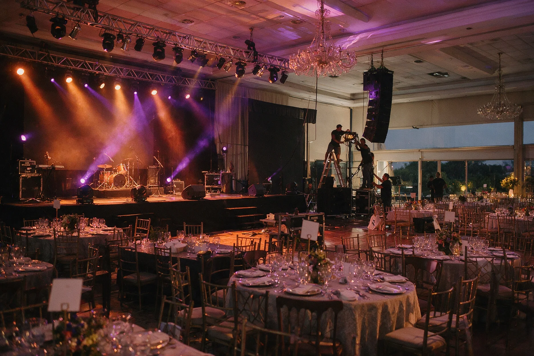 Salón armado para una fiesta, con las mesas puestas y el escenario iluminado